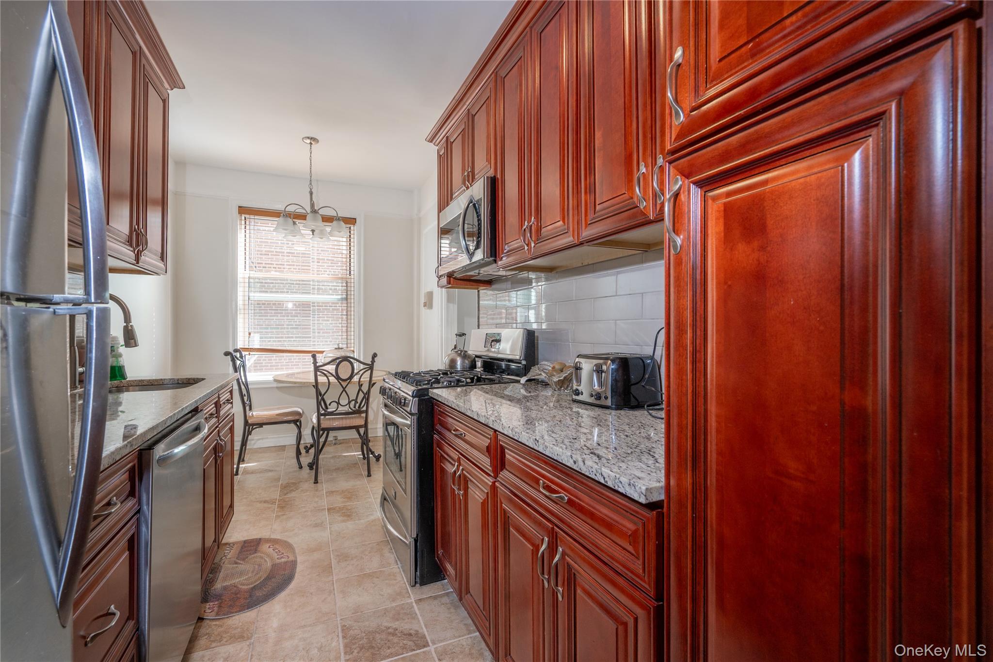 1468 Midland Avenue, Unit 4D Bronxville, NY 10708 - Photo 14 of 24 Kitchen with appliances with stainless steel finishes, pendant lighting, tasteful backsplash, a chandelier, and light stone countertops