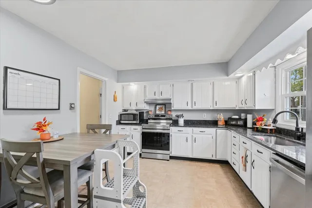 a kitchen with stainless steel appliances granite countertop a stove top oven a sink dishwasher and white cabinets with wooden floor