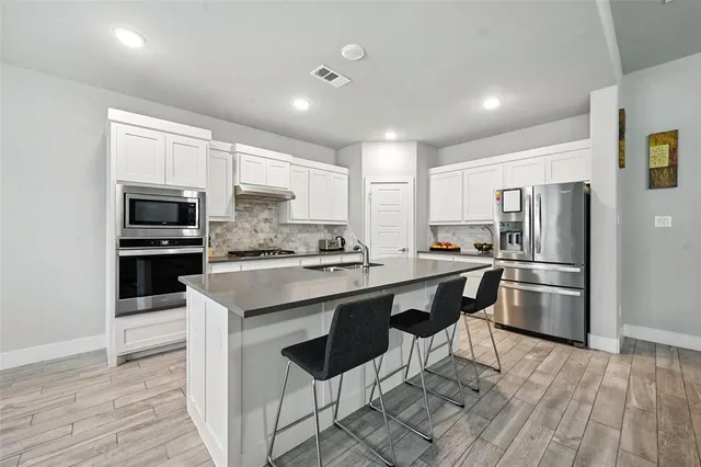 a kitchen with stainless steel appliances a stove a sink dishwasher a refrigerator and a stove with wooden floor