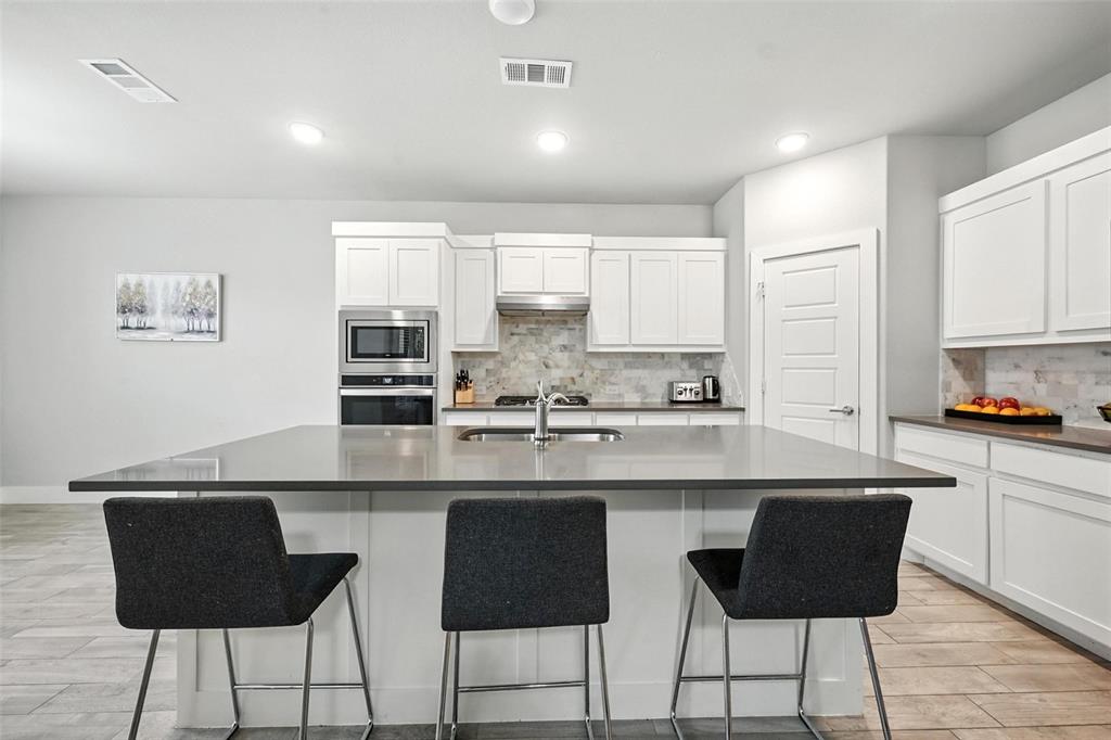 113 Nathan Drive Princeton, TX 75407 - Photo 12 of 39 a kitchen with stainless steel appliances kitchen island granite countertop a stove a sink and white cabinets with wooden floor