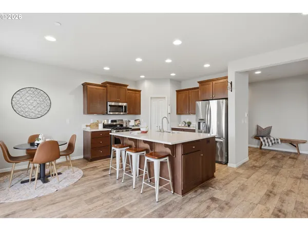 a open kitchen with stainless steel appliances granite countertop a stove top oven a sink dishwasher a dining table and chairs with wooden floor