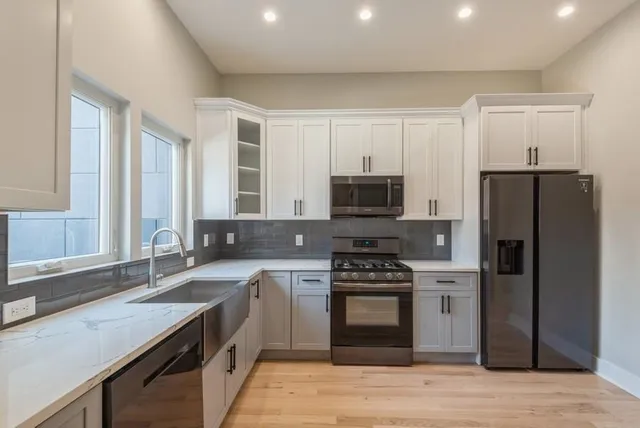 a large kitchen with stainless steel appliances granite countertop a stove a sink dishwasher a refrigerator and a microwave oven with wooden floor
