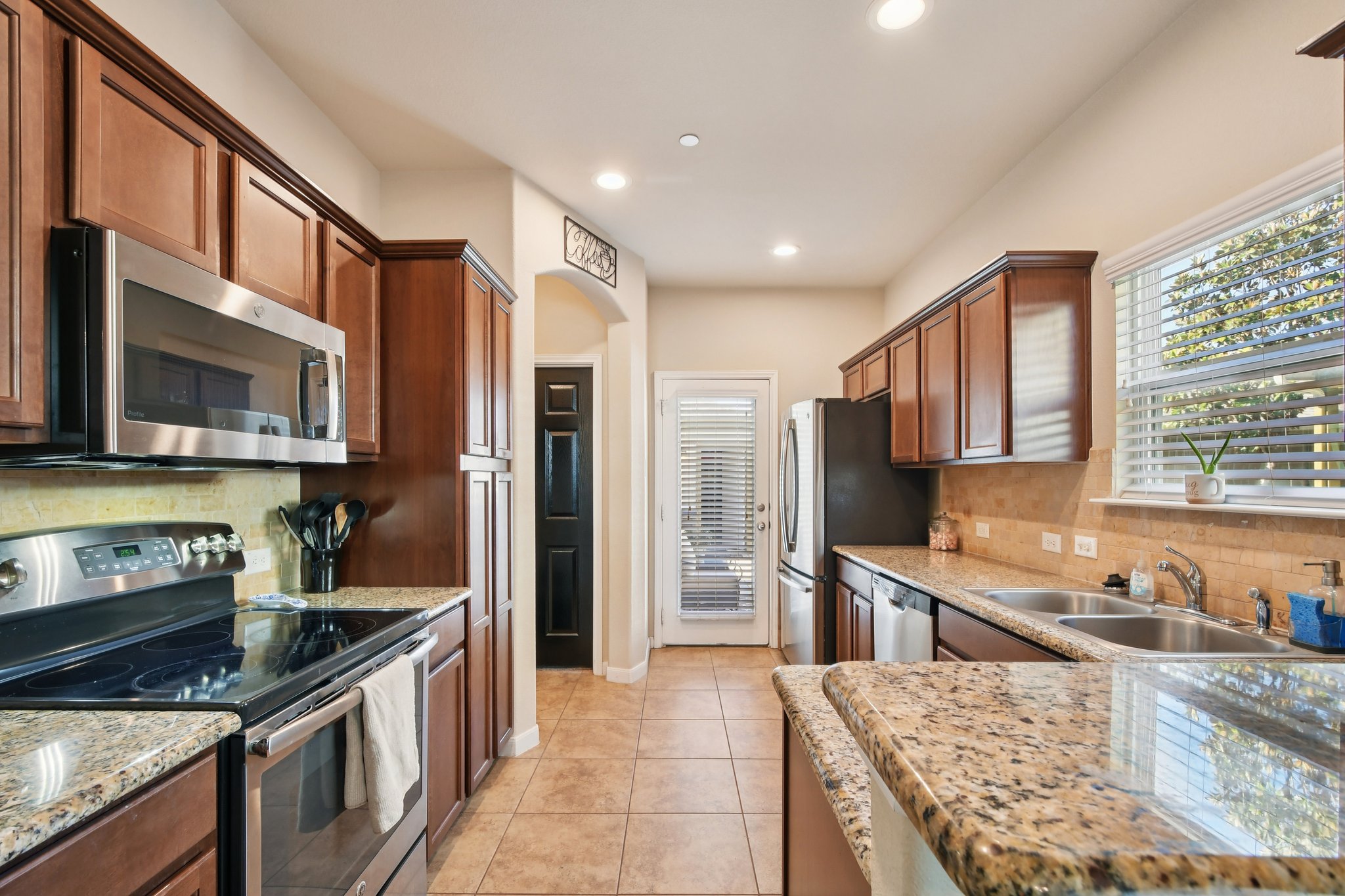 616 Lookout Tree Lane Round Rock, TX 78664 - Photo 8 of 39 Kitchen featuring stainless steel appliances, backsplash, light stone countertops, light tile patterned floors, and wood finish cabinetry