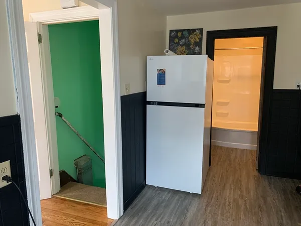 a view of a living room with a refrigerator and wooden floor