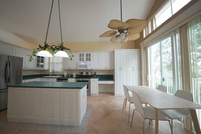 a kitchen with stainless steel appliances granite countertop a dining table chairs a refrigerator and a chandelier