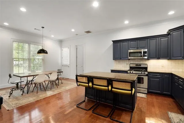 a kitchen with stainless steel appliances granite countertop a stove top oven a sink a dining table and chairs with wooden floor