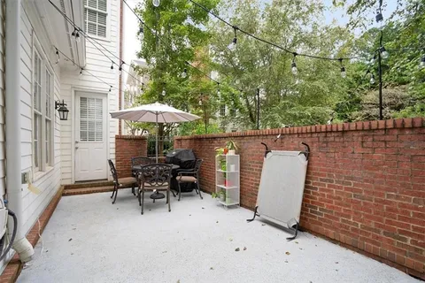 a view of a patio with table and chairs under an umbrella with large trees
