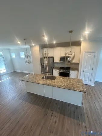 a large kitchen with stainless steel appliances a large counter top a wooden floors and a view of living room