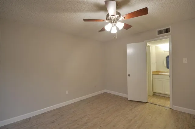 an empty room with a chandelier fan and wooden floor