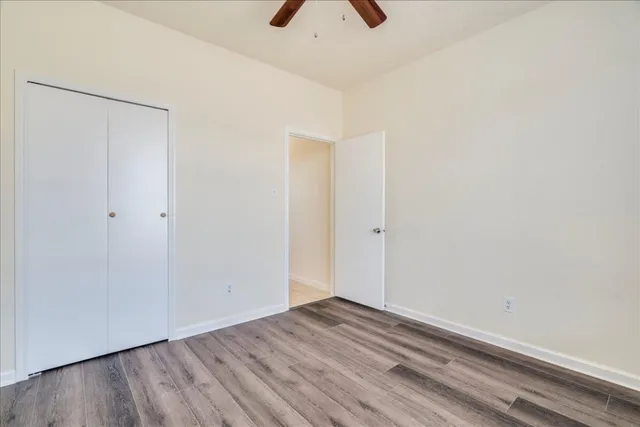 a view of an empty room with wooden floor and a ceiling fan