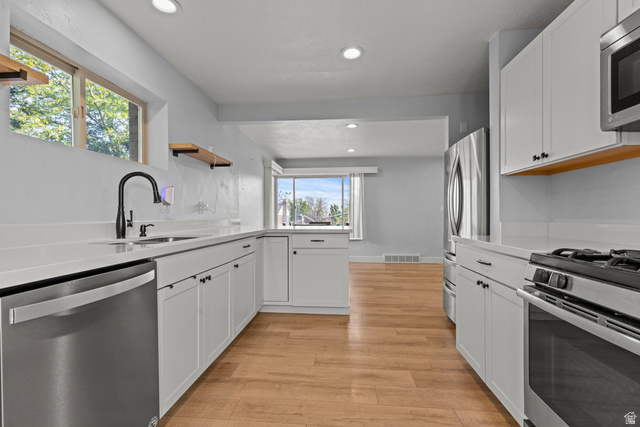 2101 West 3900th Street South Roy, UT 84067 - Photo 22 of 36 Modern kitchen featuring white shaker cabinetry, stainless steel appliances, a black gooseneck faucet, light wood-finish flooring, and recessed lighting