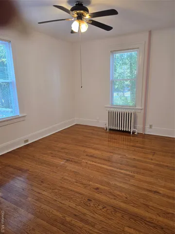 an empty room with wooden floor chandelier fan and windows