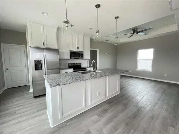 a kitchen with stainless steel appliances granite countertop a refrigerator a sink dishwasher a stove and white cabinets with wooden floor