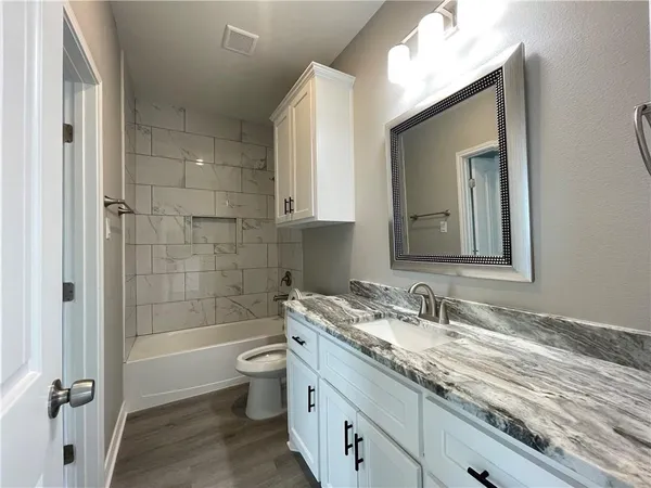 a bathroom with a granite countertop sink toilet mirror and bathtub