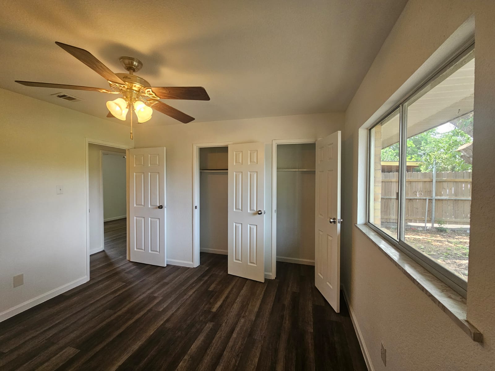 1401 Trinity Street Lockhart, TX 78644 - Photo 15 of 31 Spacious interior featuring wood-finish flooring, a ceiling fan with integrated lighting, a large window with a stone sill, and two sets of double-door closets