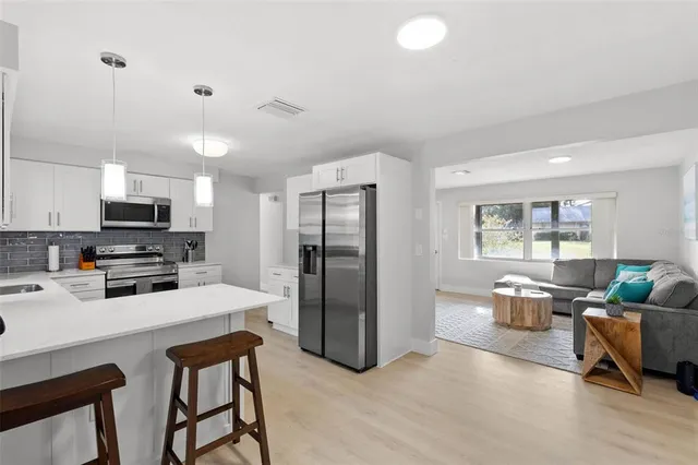 a kitchen with stainless steel appliances kitchen island granite countertop a refrigerator a stove a sink a dining table and chairs with wooden floor