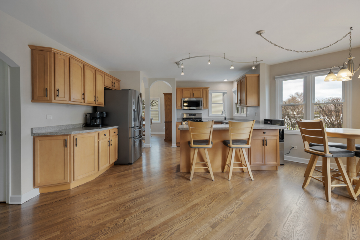 24854 Buttercup Lane Manhattan, IL 60442 - Photo 13 of 36 a kitchen with stainless steel appliances kitchen island wooden floors and white cabinets