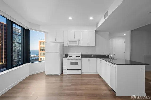 a kitchen with granite countertop a stove a sink and white cabinets with wooden floor