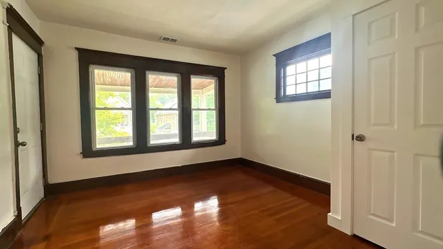 a view of an empty room with wooden floor and a window