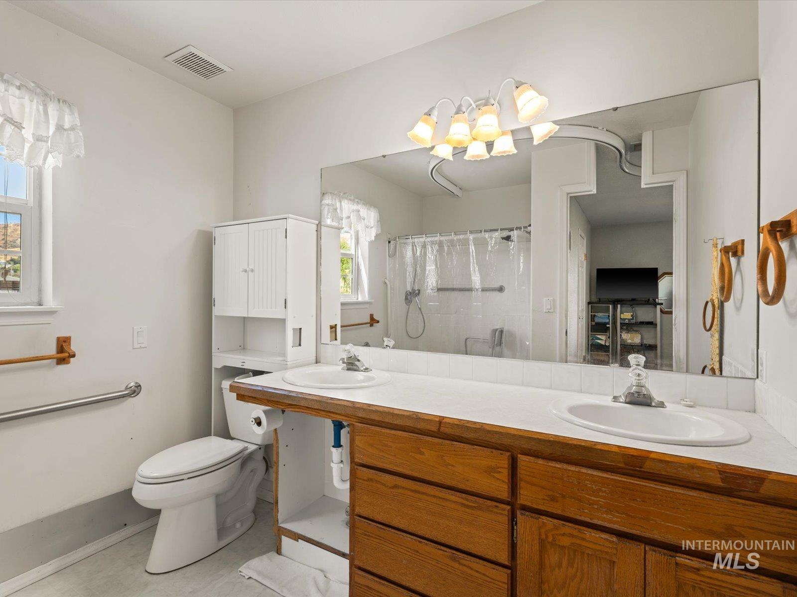 3540 Wills Road Emmett, ID 83617 - Photo 18 of 36 Bathroom featuring a double vanity with wood cabinetry, a large wall-mounted mirror, and a shower with white tile surround