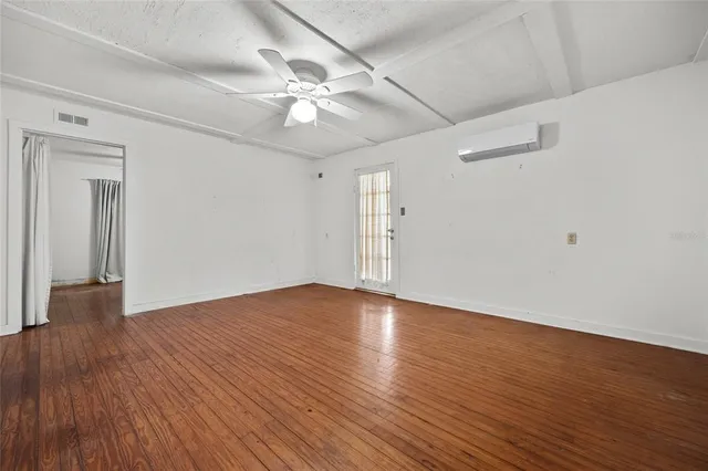 an empty room with wooden floor chandelier fan and windows