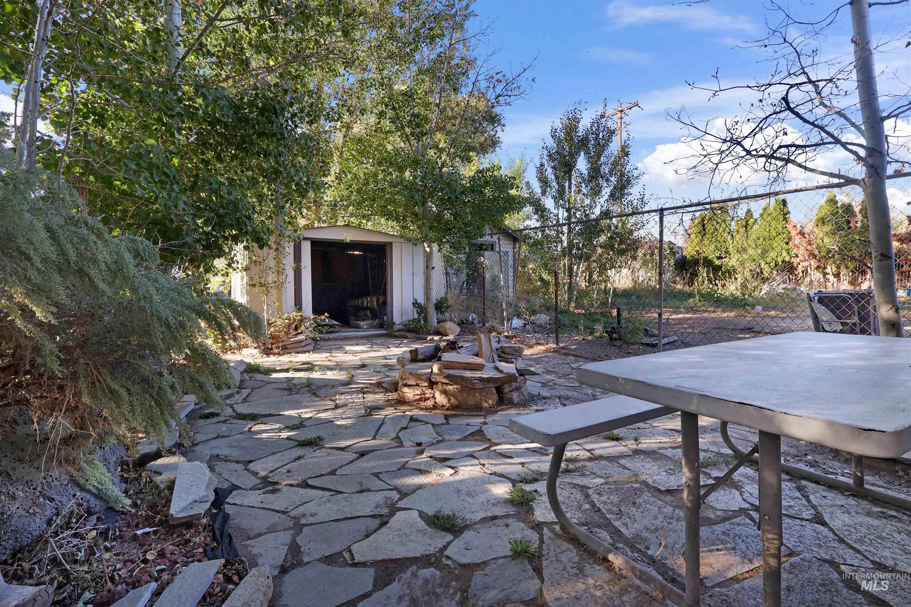 1009 9th Street Rupert, ID 83350 - Photo 24 of 28 Stone patio with a built-in fire pit, surrounded by mature trees and lush plantings