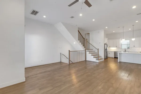 an empty room with wooden floor and kitchen view