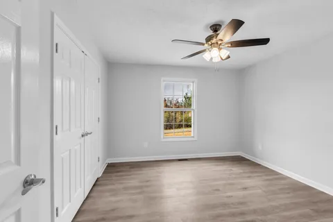 an empty room with wooden floor fan and windows