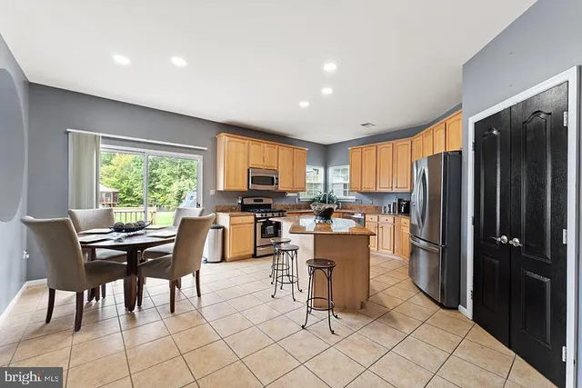 a kitchen with stainless steel appliances kitchen island granite countertop a refrigerator a stove a dining table and chairs with wooden floor