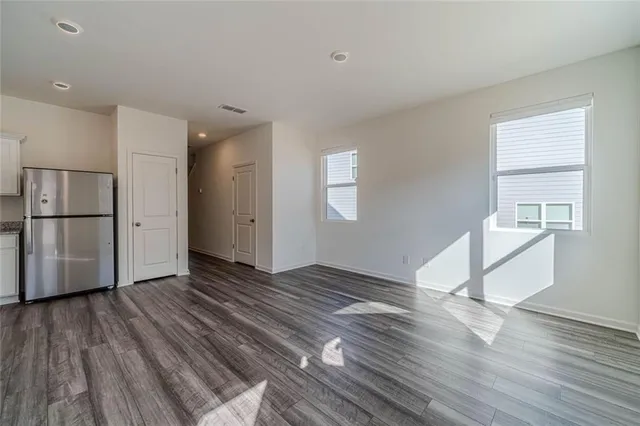 a view of empty room with wooden floor and kitchen
