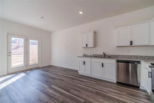 a kitchen with granite countertop a stove a sink and white cabinets with wooden floor