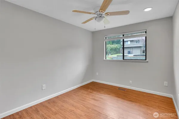 an empty room with wooden floor chandelier fan and windows