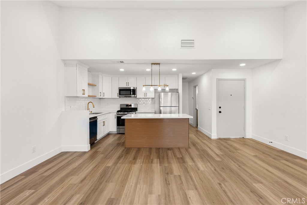 87 Tennessee Street, Unit C Redlands, CA 92373 - Photo 12 of 32 a large room with kitchen island a sink dishwasher stove and white cabinets with wooden floor