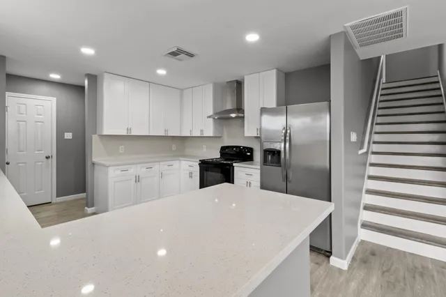 a open kitchen with stainless steel appliances kitchen island a sink dishwasher a refrigerator and white cabinets with wooden floor