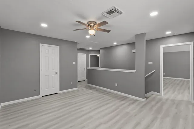 a view of an empty room with wooden floor and a ceiling fan
