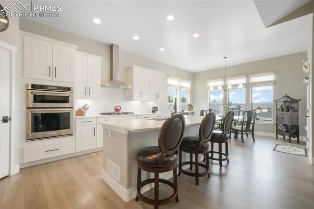 a kitchen with stainless steel appliances granite countertop a stove top oven a sink a dining table and chairs with wooden floor