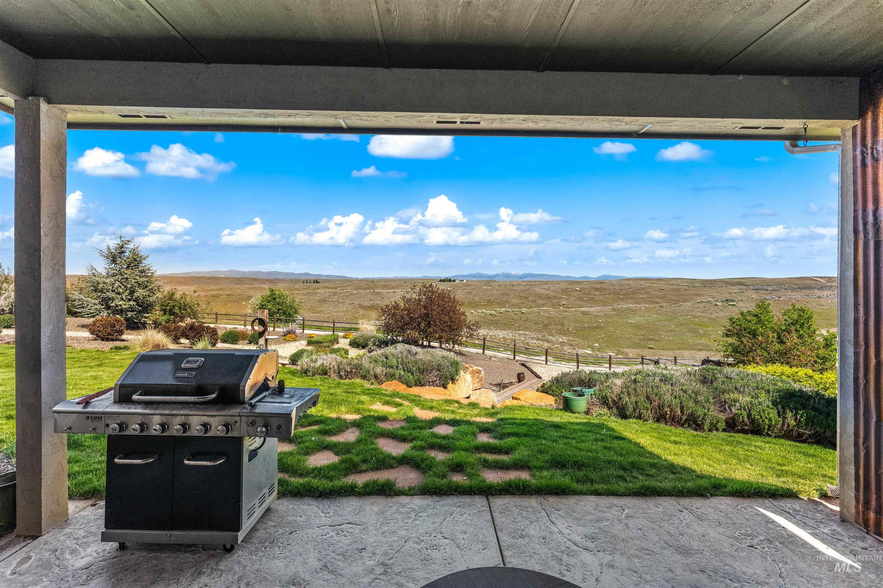 7521 North Grand Ridge Lane Eagle, ID 83616 - Photo 46 of 50 Covered patio with stamped concrete flooring, overlooking a terraced yard with mature landscaping and distant open fields