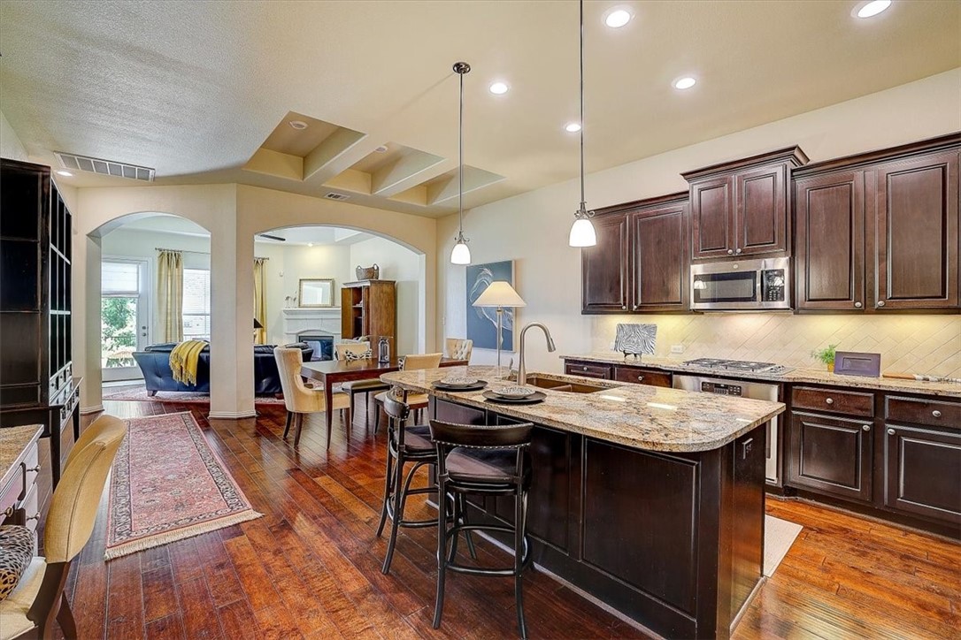a kitchen with stainless steel appliances granite countertop wooden cabinets a stove a sink a dining table and chairs