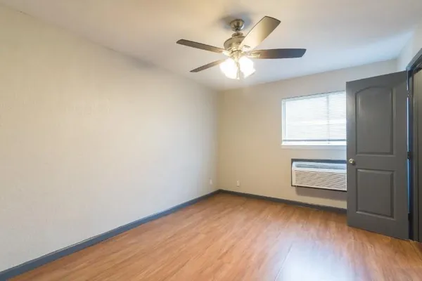 an empty room with wooden floor chandelier fan and windows