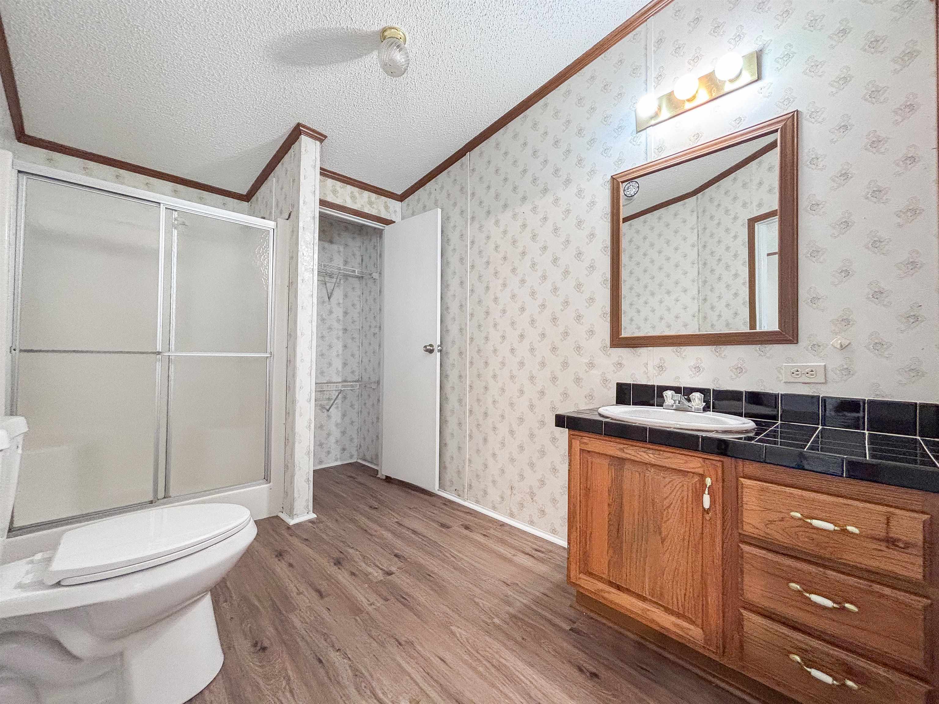 2847 Holly Grove Road Covington, TN 38019 - Photo 20 of 36 Bathroom featuring wood-finish flooring, a wood vanity with a drop-in sink, a black tiled countertop, a framed wall mirror, and a glass-enclosed shower