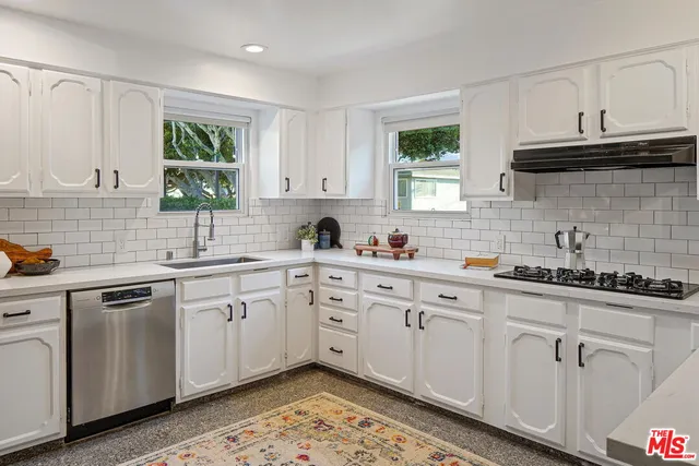 a large white kitchen with stainless steel appliances granite countertop a stove a sink dishwasher and white cabinets with wooden floor