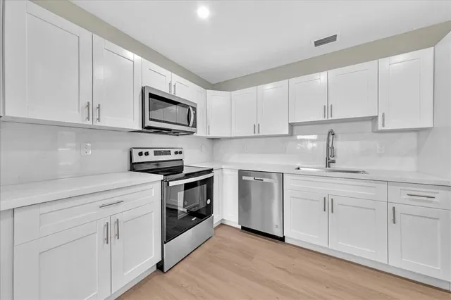 a kitchen with white cabinets white stainless steel appliances and sink
