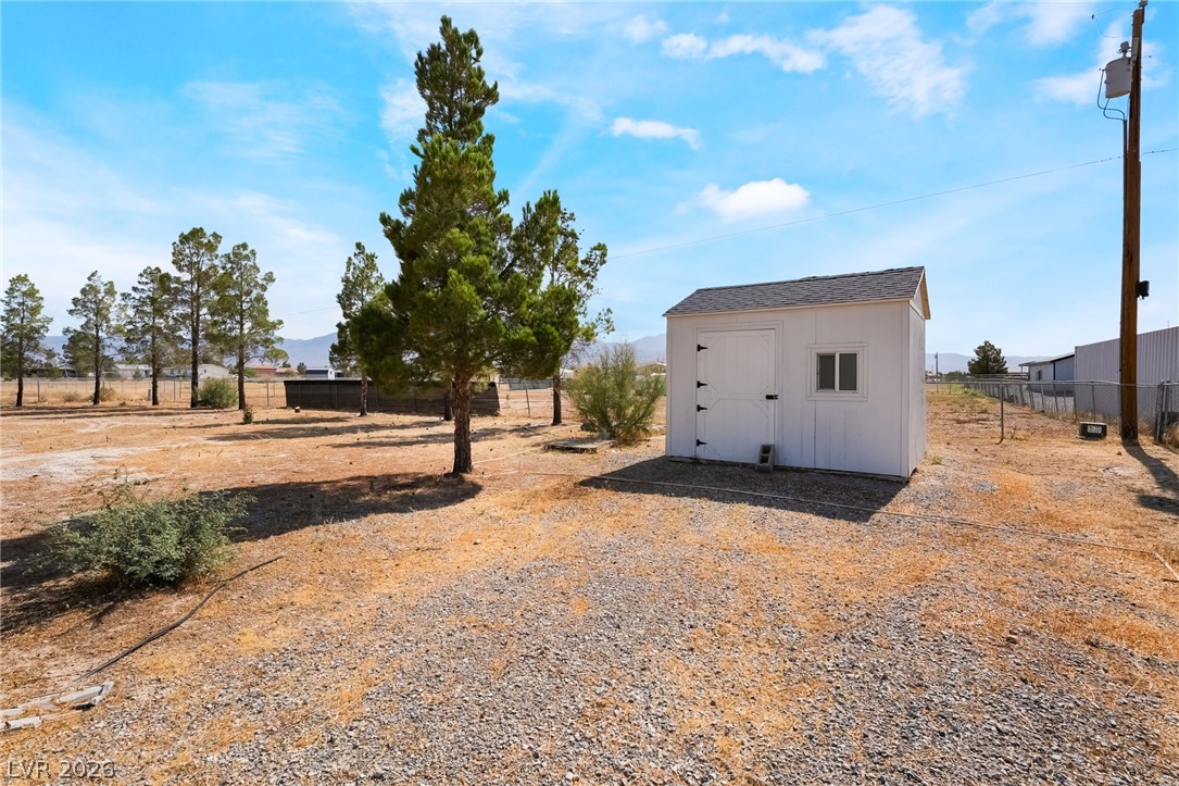 3631 South Blagg Road Pahrump, NV 89048 - Photo 36 of 47 A quaint storage shed stands ready on a vast, naturally illuminated lot, framed by distant mountains and a scattering of evergreens.