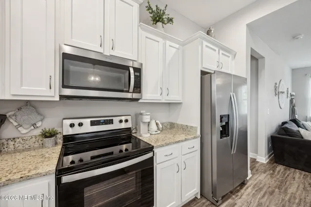 a large white kitchen with kitchen island a refrigerator a stove a sink dishwasher a oven with white cabinets and wooden floor