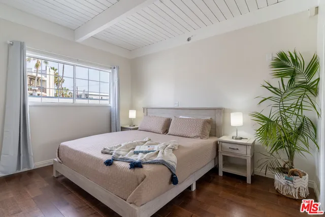 a bedroom with a bed table flowerpot and window