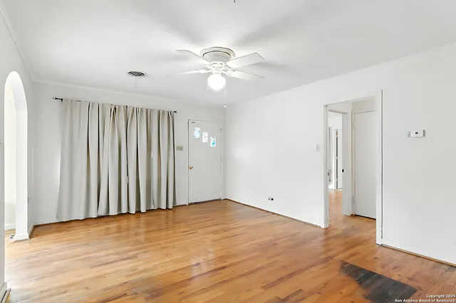 an empty room with wooden floor fan and windows