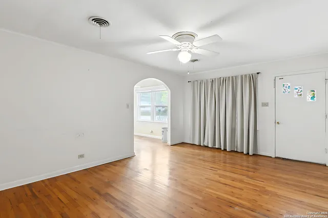 an empty room with wooden floor chandelier fan and windows