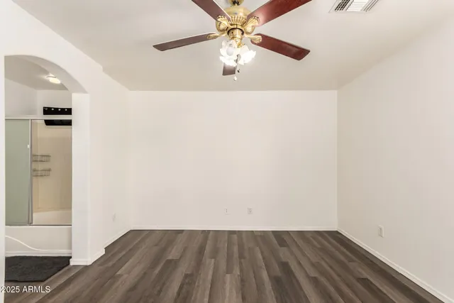 an empty room with wooden floor chandelier fan and windows