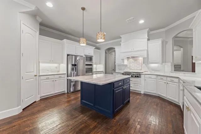 a kitchen with stainless steel appliances granite countertop a refrigerator a sink dishwasher a oven and white cabinets with wooden floor