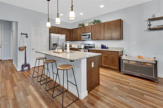 a kitchen with stainless steel appliances granite countertop a sink a stove a refrigerator and island with wooden floor